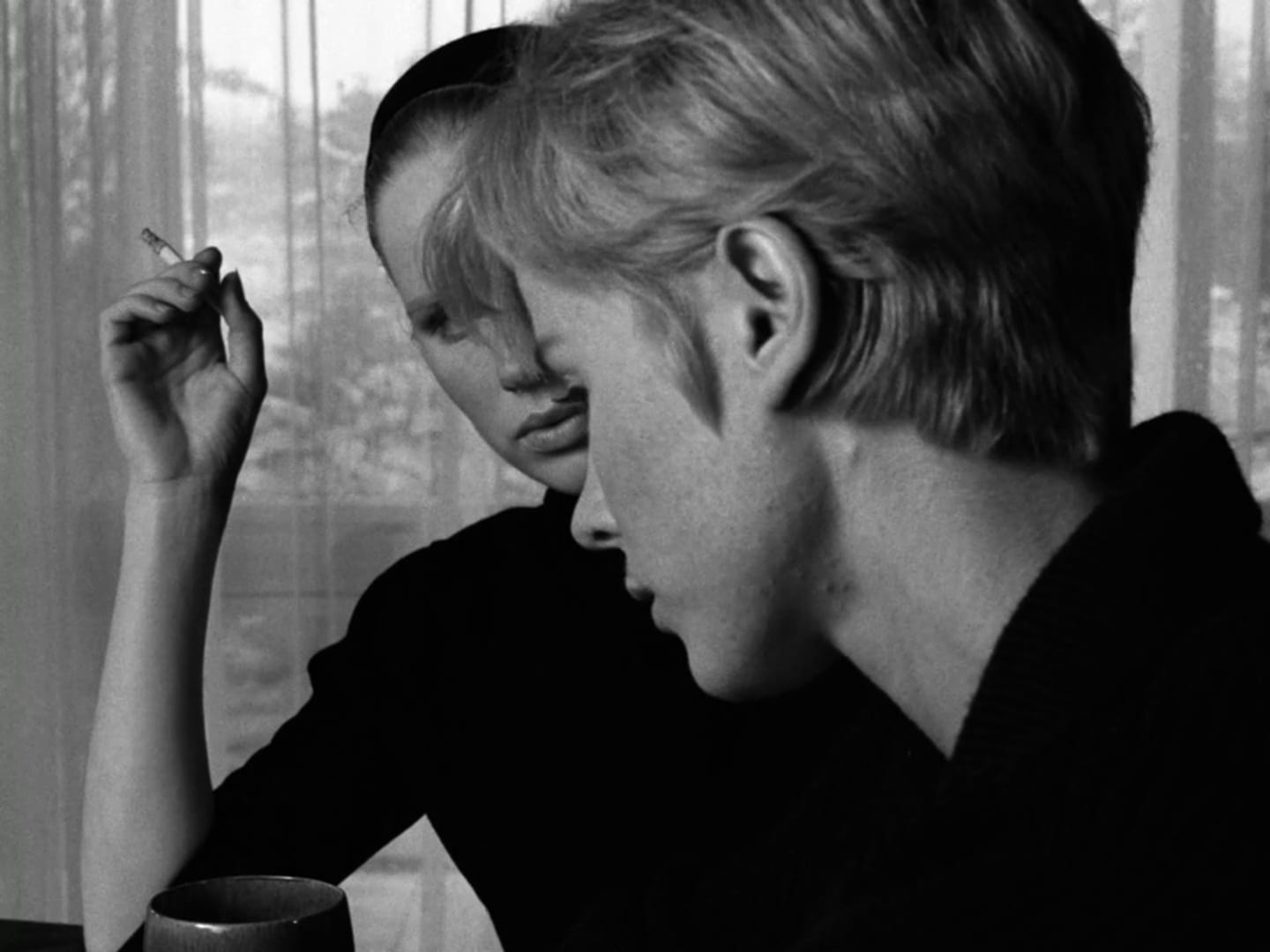 Scena in bianco e nero di due donne sedute una accanto all’altra, una con una sigaretta in mano, in un momento di silenzio e tensione emotiva